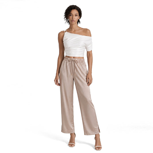 Woman wearing champagne beige satin wide leg pants with a high drawstring waist, styled with a white one shoulder crop top.