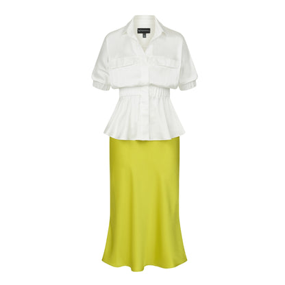 Front view of a white silky viscose peplum blouse with elastic waist, short puff sleeves and concealed buttons, paired with a lime green satin midi skirt